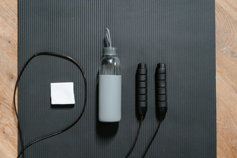 Flatlay of jump rope, water bottle, and towel on a black yoga mat.